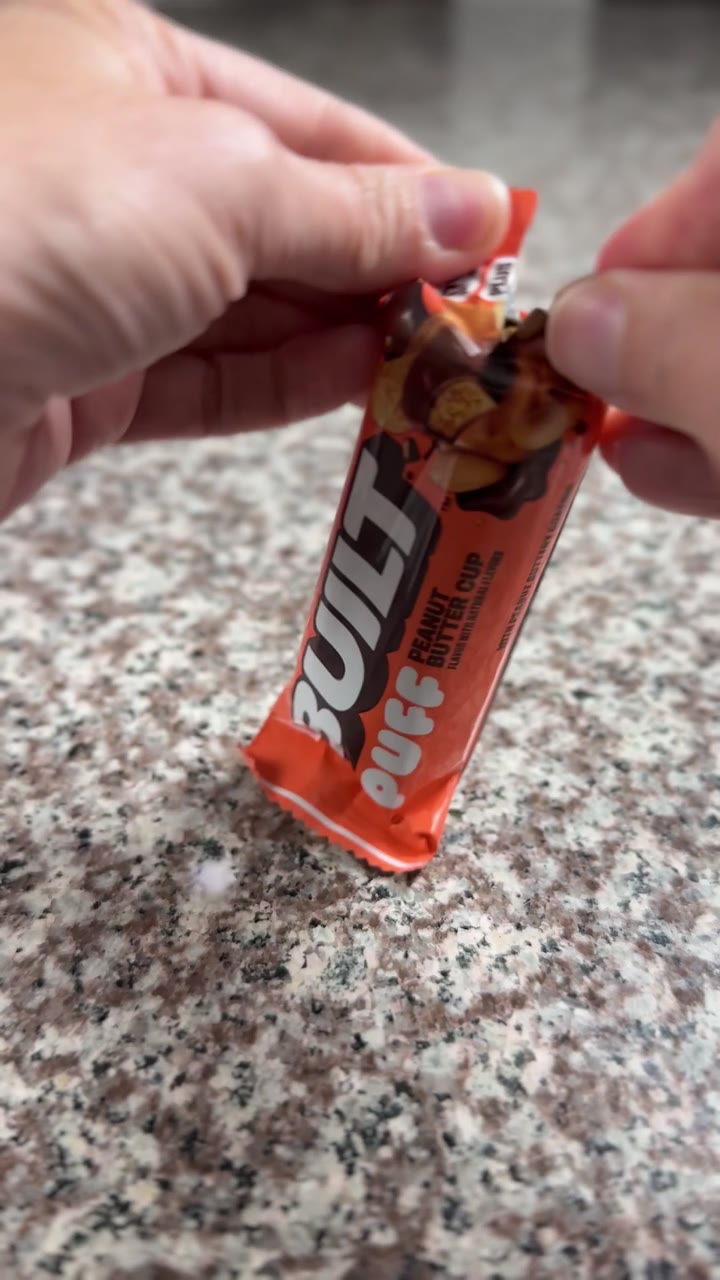 A BUILT protein bar being unwrapped over a kitchen counter.